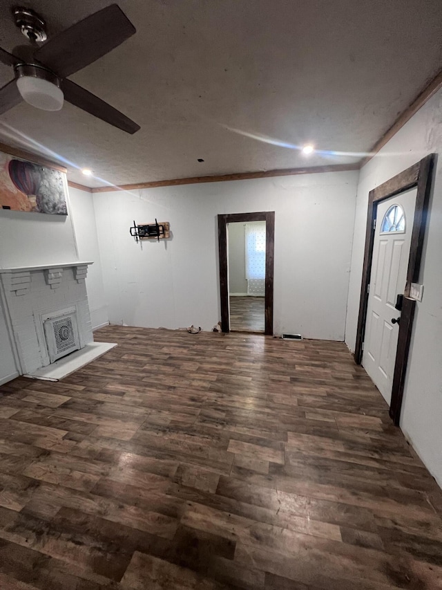 unfurnished living room with ceiling fan, a fireplace, crown molding, and dark wood-type flooring