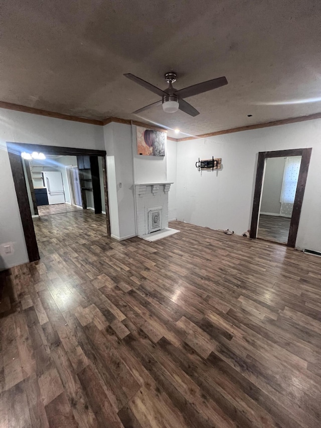 unfurnished living room featuring crown molding, dark wood finished floors, a fireplace, and a ceiling fan