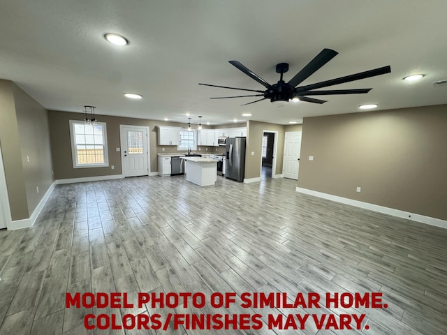 unfurnished living room featuring light wood-type flooring, a sink, a ceiling fan, and baseboards