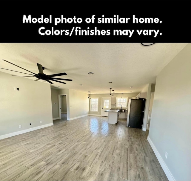 unfurnished living room featuring light wood-type flooring, a textured ceiling, baseboards, and a ceiling fan