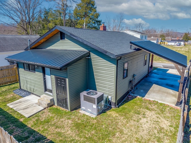 view of side of property with a shingled roof, central AC unit, a chimney, fence, and a yard