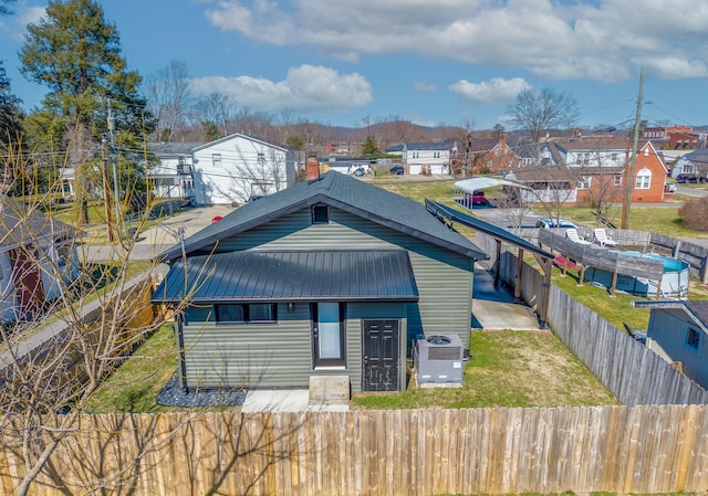 view of front of house with metal roof, central AC unit, a fenced backyard, a front lawn, and a chimney