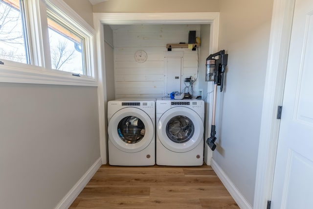 clothes washing area featuring washer and dryer, wooden walls, light wood-type flooring, laundry area, and baseboards