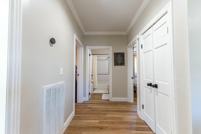 corridor featuring baseboards, light wood-type flooring, visible vents, and crown molding