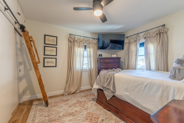 bedroom with wood finished floors, multiple windows, baseboards, and a barn door