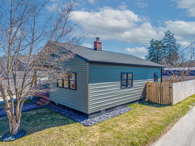 view of side of home featuring a shingled roof, a lawn, a chimney, and fence