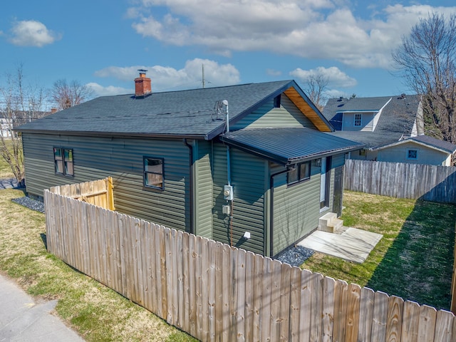 exterior space with entry steps, a fenced backyard, a yard, roof with shingles, and a chimney