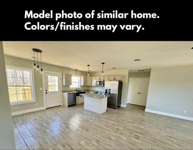 kitchen featuring appliances with stainless steel finishes, open floor plan, a center island, light wood-style floors, and a sink