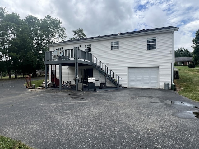 rear view of property featuring aphalt driveway, central air condition unit, a deck, a garage, and stairs