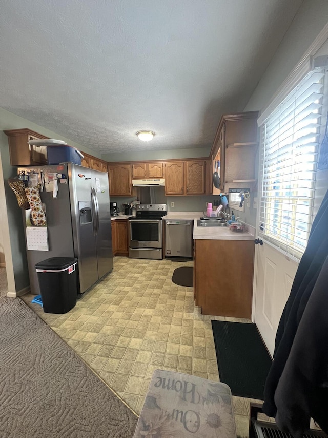 kitchen with brown cabinetry, appliances with stainless steel finishes, light countertops, under cabinet range hood, and a sink