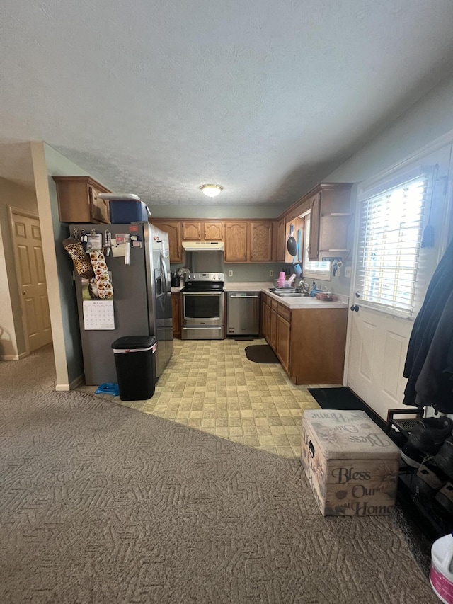 kitchen featuring brown cabinets, stainless steel appliances, light colored carpet, light countertops, and a sink