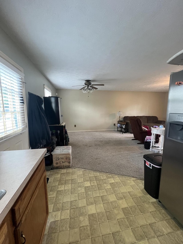 living area with ceiling fan, a textured ceiling, and light colored carpet