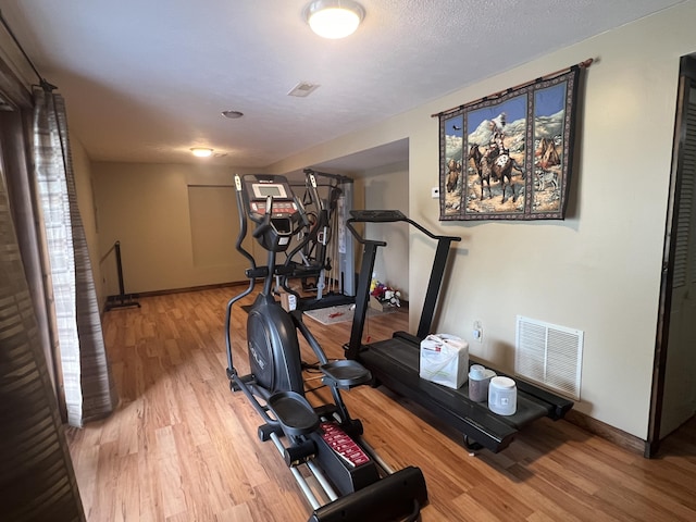 exercise area with wood finished floors, visible vents, and baseboards