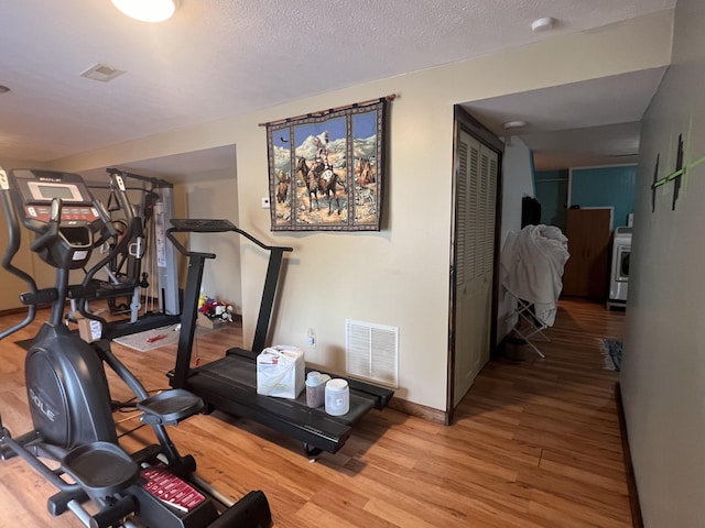 exercise area featuring baseboards, a textured ceiling, visible vents, and wood finished floors