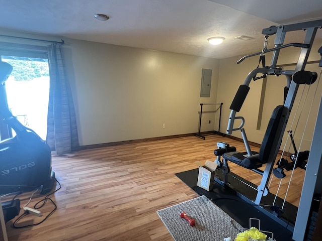 workout room featuring light wood-style floors, electric panel, baseboards, and a textured ceiling