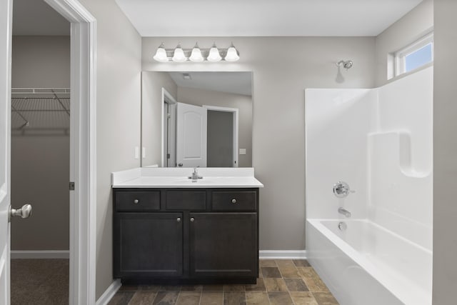 full bathroom with baseboards, stone finish flooring, bathtub / shower combination, a walk in closet, and vanity