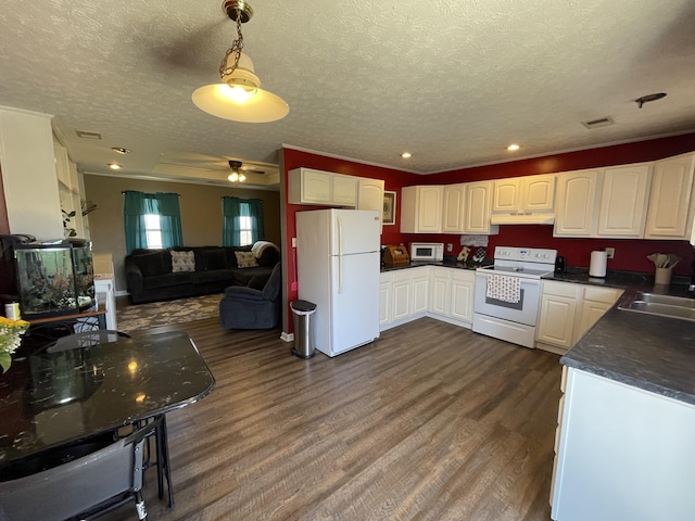 kitchen featuring white appliances, dark countertops, dark wood-type flooring, under cabinet range hood, and a sink