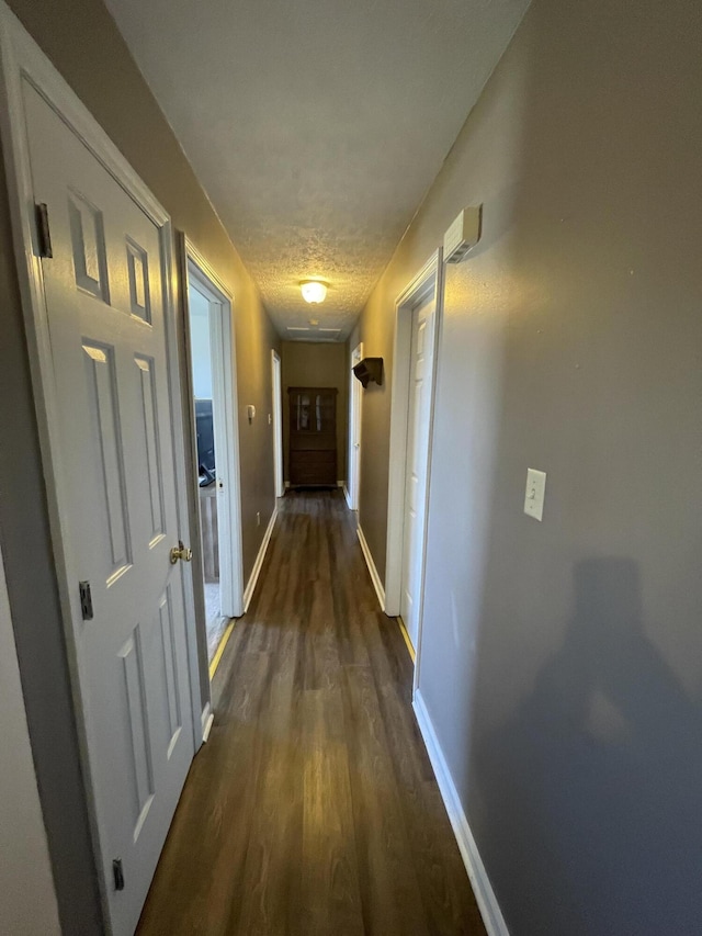 corridor with baseboards, dark wood-type flooring, and a textured ceiling