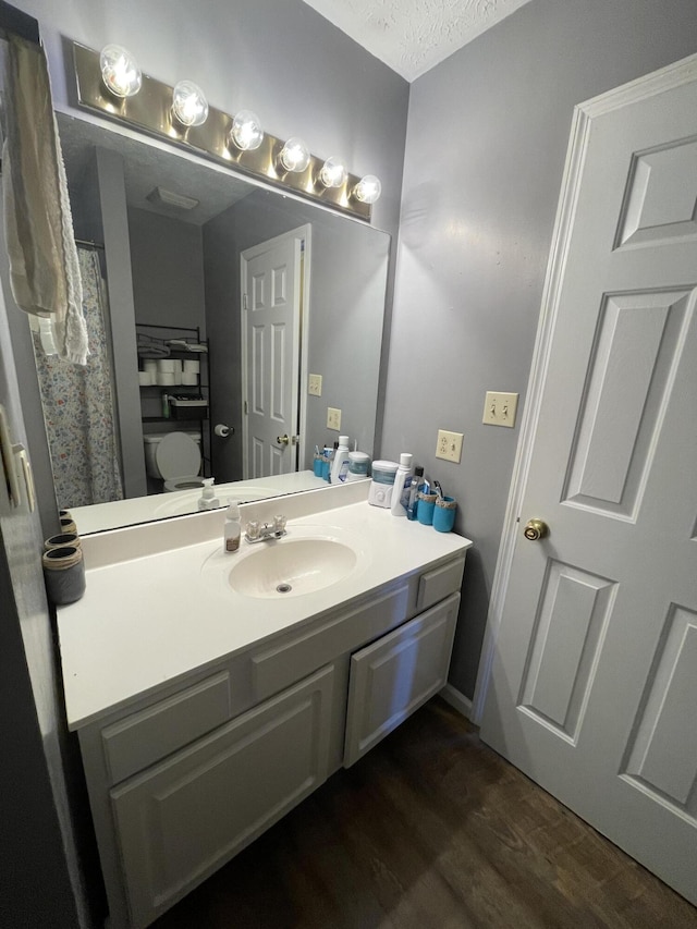 full bath with a textured ceiling, toilet, wood finished floors, and vanity