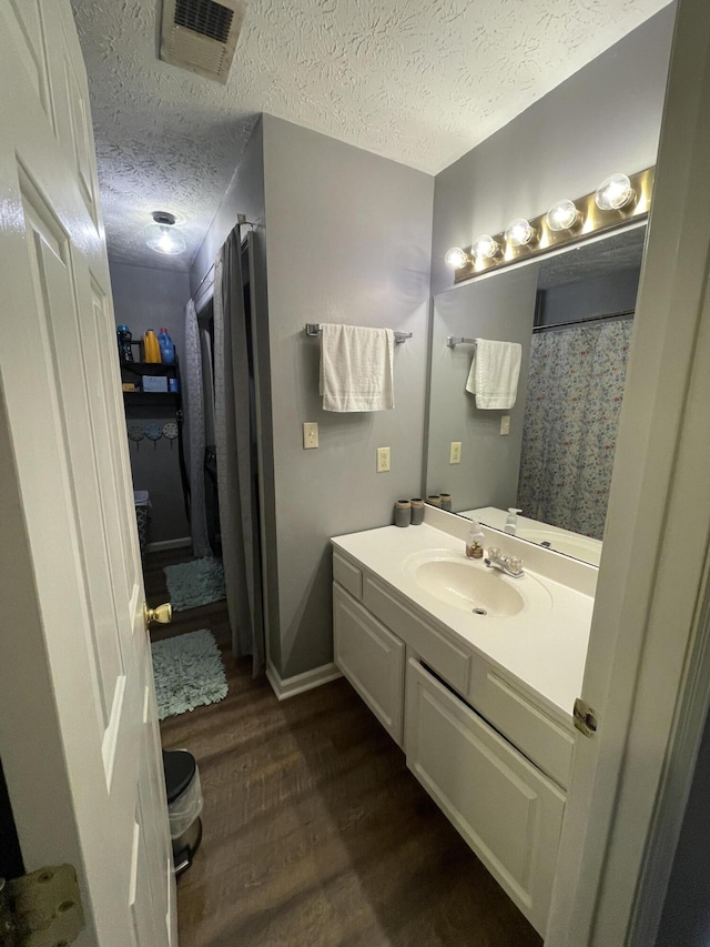 full bath with a textured ceiling, vanity, wood finished floors, and visible vents