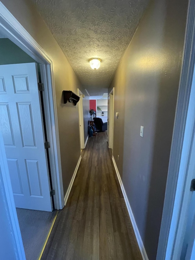 hallway with baseboards, a textured ceiling, and wood finished floors