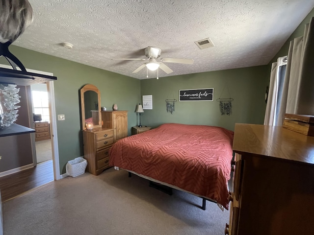 carpeted bedroom featuring ceiling fan, a textured ceiling, visible vents, and baseboards