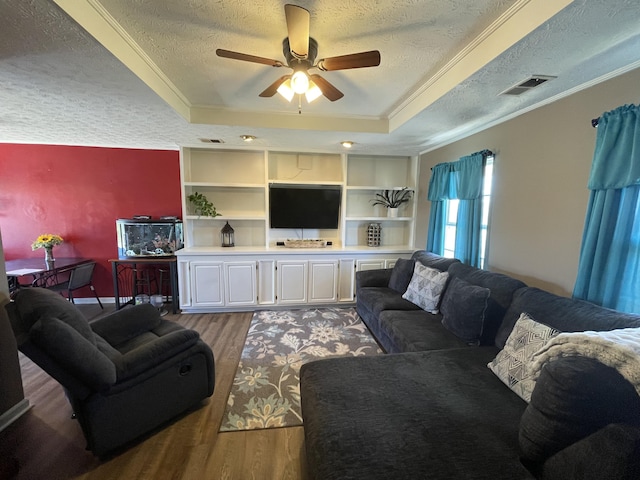 living room featuring visible vents, a raised ceiling, wood finished floors, crown molding, and a textured ceiling