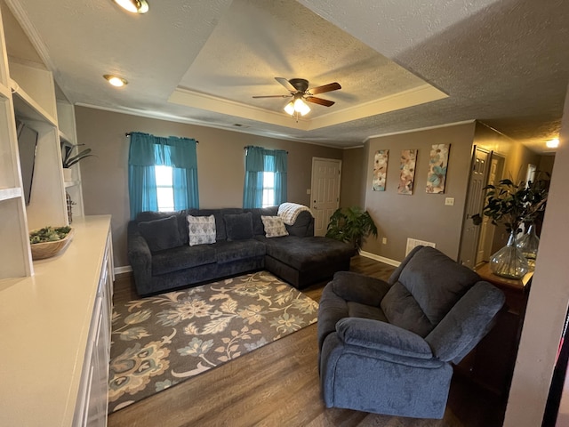 living room with a textured ceiling, wood finished floors, a raised ceiling, and baseboards