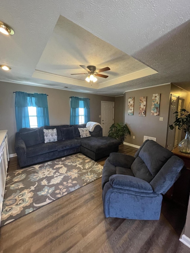 living room featuring plenty of natural light, a textured ceiling, a tray ceiling, and wood finished floors