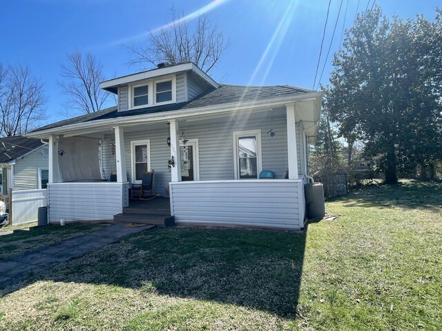 bungalow featuring a front yard, covered porch, roof with shingles, and fence