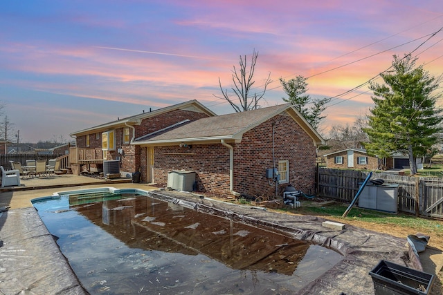 pool at dusk featuring a patio, central AC, and a fenced backyard