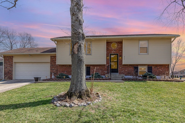 raised ranch with a front yard, an attached garage, brick siding, and concrete driveway