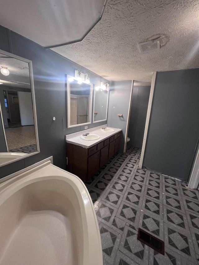 full bath with a bath, a textured ceiling, vanity, and visible vents