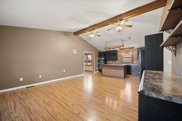 unfurnished living room featuring light wood-type flooring, visible vents, a ceiling fan, baseboards, and vaulted ceiling with beams