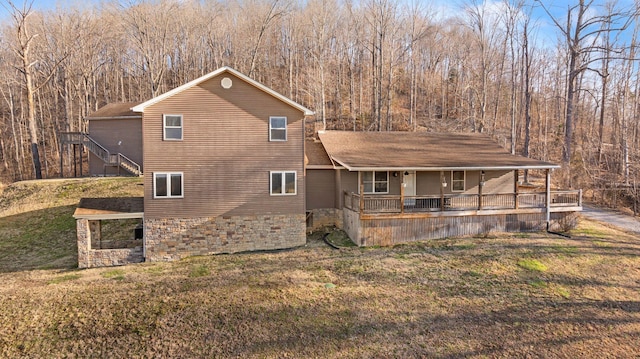 rear view of property featuring covered porch, a view of trees, stairs, and a yard