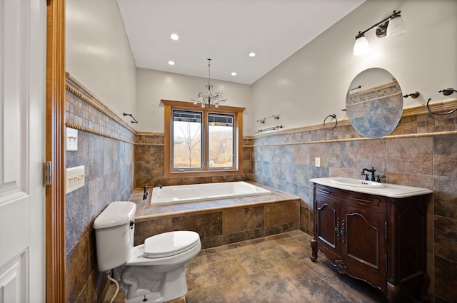 bathroom featuring a wainscoted wall, toilet, vanity, a bath, and tile walls