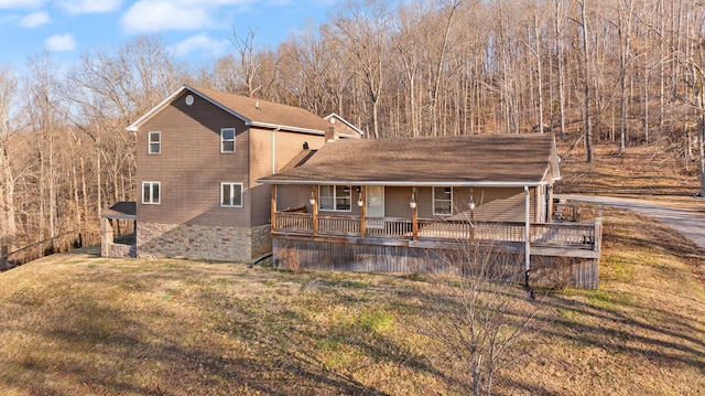 rear view of property with a porch, a yard, and roof with shingles