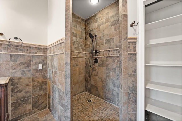 full bathroom with a wainscoted wall, tile walls, and a tile shower