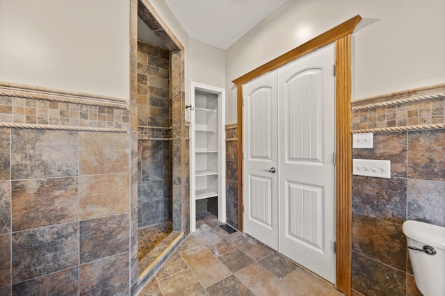 bathroom with a closet, toilet, a tile shower, and tile walls