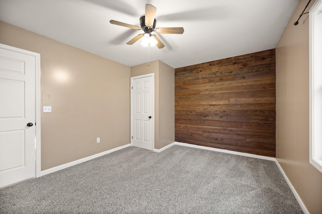 unfurnished room featuring carpet flooring, baseboards, wooden walls, and a ceiling fan