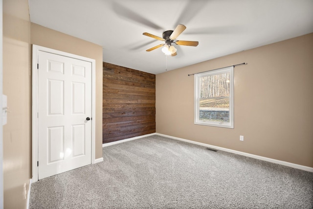 carpeted empty room with wooden walls, a ceiling fan, visible vents, and baseboards