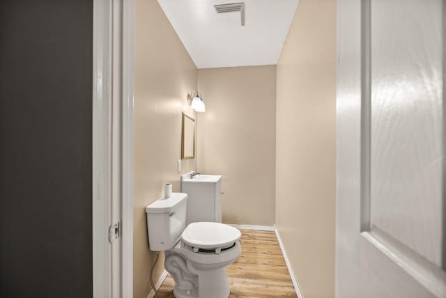 half bathroom with vanity, wood finished floors, visible vents, baseboards, and toilet