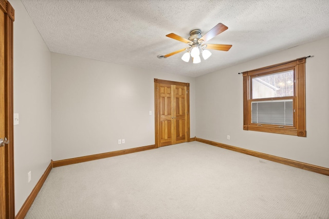 empty room with light colored carpet, a textured ceiling, a ceiling fan, and baseboards