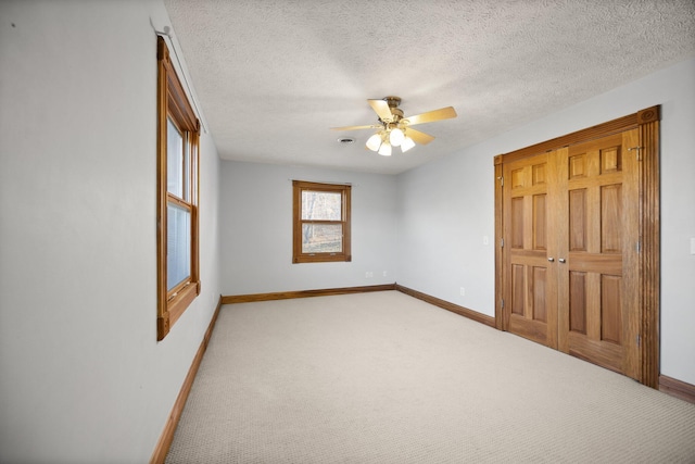 unfurnished bedroom featuring baseboards, light colored carpet, ceiling fan, and a textured ceiling