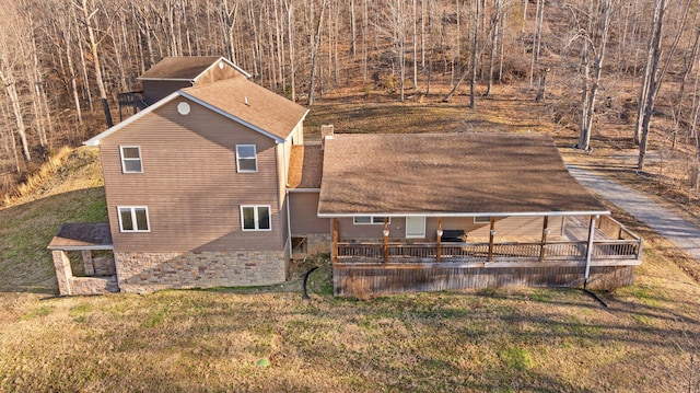 view of side of property featuring a wooden deck, a lawn, and a shingled roof