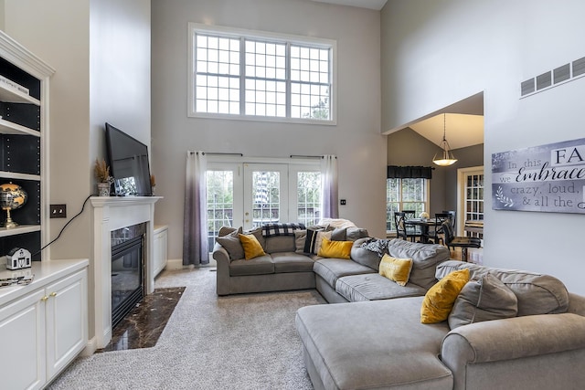 living area featuring light carpet, a premium fireplace, a towering ceiling, and visible vents