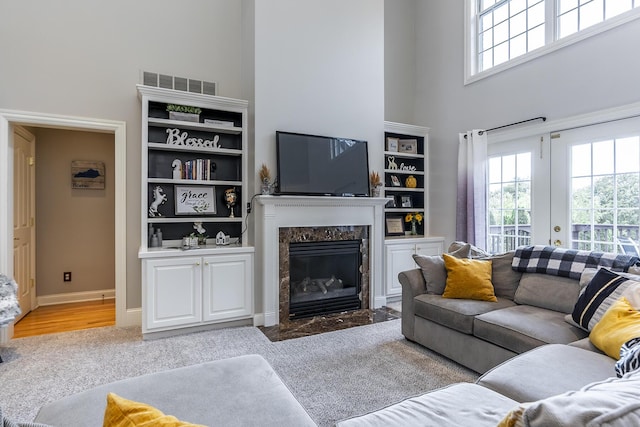 living room with carpet, visible vents, a high ceiling, and a premium fireplace