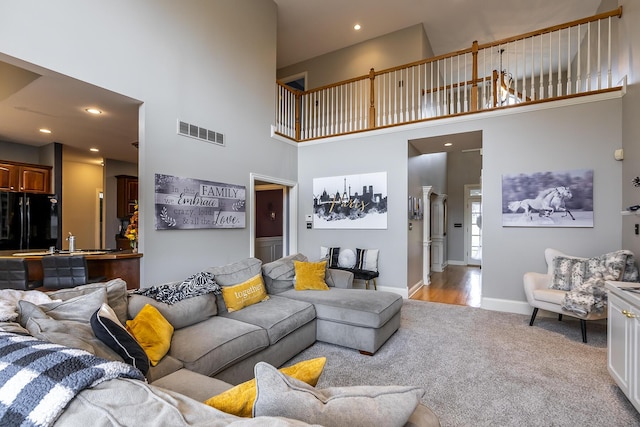 carpeted living room with a towering ceiling, baseboards, visible vents, and recessed lighting