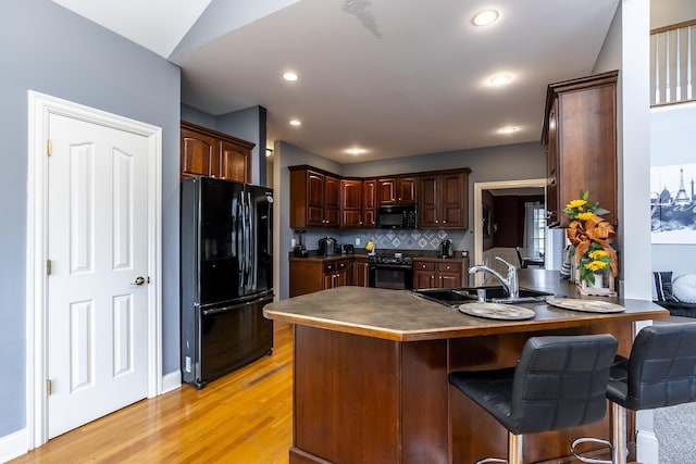 kitchen with light wood finished floors, dark countertops, a peninsula, black appliances, and a sink