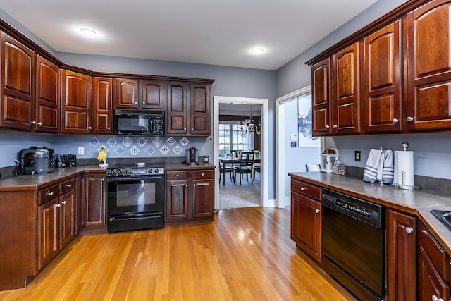 kitchen featuring decorative backsplash, dark countertops, light wood-style flooring, black appliances, and a chandelier